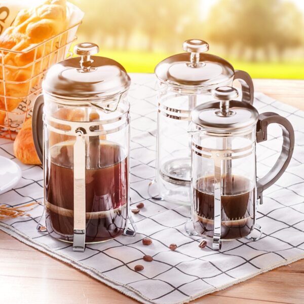 Three sizes of stainless steel, heat-resistant glass French presses sit on a white tea towel with black grid lines
