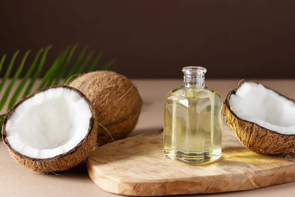 glass bottle of oil beside open coconuts